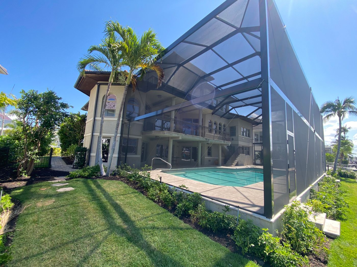 A wide view of a beautiful pool in Naples, Florida with a large screen enclosure.